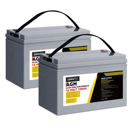 Two large, rectangular gray batteries equipped with black carrying handles and vibrant yellow, red, and white labels displaying "Giantz AGM Deep Cycle Battery 12V 100Ah x2 Box Portable Solar Caravan Camping." Both portable deep cycle batteries feature specifications listed on their labels, emphasizing the advanced AGM technology.