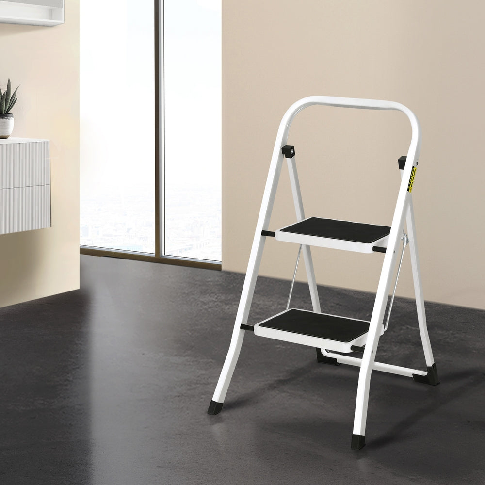 A white, two-step foldable ladder with black steps and non-slip rubber feet stands on a plain white background. The Giantz 2 Step Ladder Multi-Purpose Folding Steel Light Weight Platform has a simple, lightweight metal frame designed for household use.