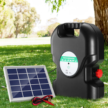 A black, portable Giantz Fence Energiser 20KM Solar Powered 1.2J Electric with a handle on top ensures livestock protection. It's connected to a small solar panel by a cable, employing two red alligator clips attached to black and red wires in front of the waterproof energizer.