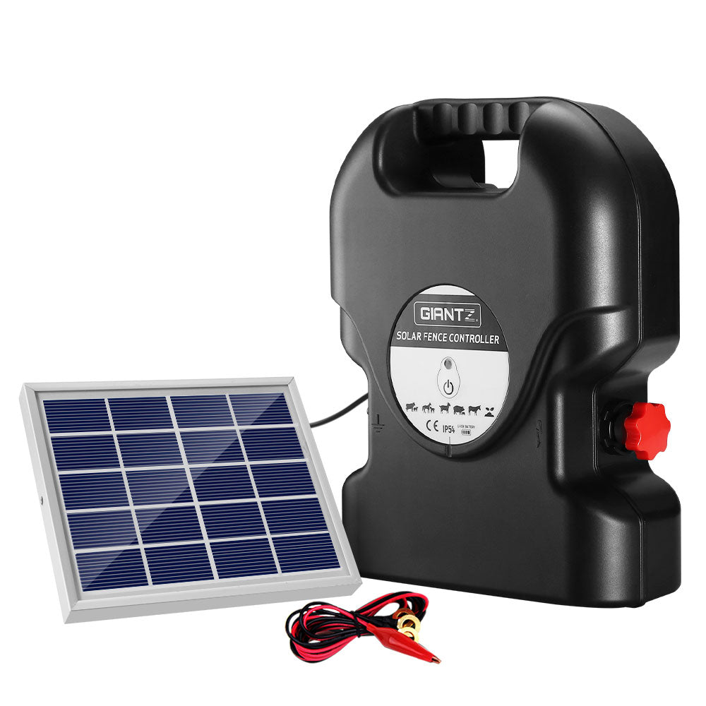 A Giantz Fence Energiser 15KM Solar Powered 0.8J Electric with a handle labeled "GIANTZ" is connected to a small solar panel. Two red and black alligator clip cables are placed beside the controller. The setup is ideal for electric fencing purposes, providing reliable livestock protection.