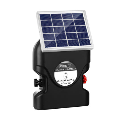 A Giantz Fence Energiser 15KM Solar Powered 0.8J Electric with a handle labeled "GIANTZ" is connected to a small solar panel. Two red and black alligator clip cables are placed beside the controller. The setup is ideal for electric fencing purposes, providing reliable livestock protection.