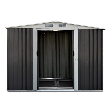 A small garden shed with its door partially open reveals garden tools inside. The text reads "Quality construction, Giantz Garden Shed 2.58x2.07M w/Metal Base Sheds Outdoor Storage Double Door Tool, designed for robust use with enhanced durability." Additional labels indicate "0.6MM Thick," "Anti-Rust," and "Galvanized steel." A green hedge is in the background.