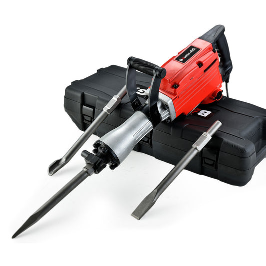 A robust, commercial-grade Tradie's Mate Baumr-AG 2200W Pro-Grade Electric Demolition Jackhammer, with a black handle rests on a closed black plastic carrying case. This 2200W jackhammer includes three chisels—one pointed and two flat—positioned beside the tool and ready for use. Its metallic components ensure it's built for heavy-duty tasks.