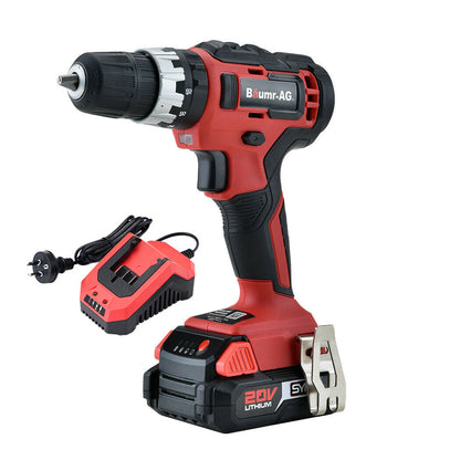 A red and black cordless drill labeled "BAUMR-AG 20V Cordless Power Drill Kit Lithium Battery Hammer Drilling with Bag" is shown from the side. The drill features TriMode technology, and an accompanying battery charger with a two-prong plug is placed beside it.