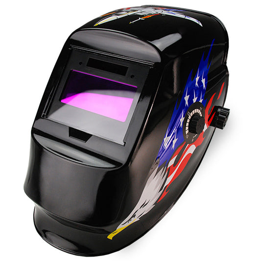 The ROSSI Solar Auto Darkening Welding Helmet ARC/TIG/MIG Welder Machine Mask is a black helmet featuring an American flag with an eagle design on the side. It boasts a rectangular viewing window with automatic tinting and a purple hue, along with an adjustable knob for fitting. This solar helmet ensures both style and functionality.