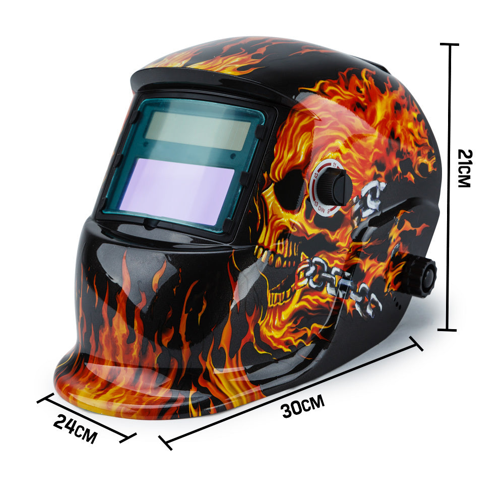 A black ROSSI Solar Auto Darkening Welding Helmet Mask MIG/ARC/TIG Welder Machine with an artistic design featuring vibrant flames and a fiery skull on the sides. This solar helmet boasts a wide viewing window with automatic tinting and an adjustable knob for optimal comfort.