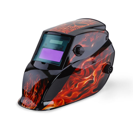 The ROSSI Solar Auto Darkening Welding Helmet Mask MIG/ARC/TIG Welder Machine features a design of realistic flames on a black background. This solar helmet boasts a large viewing window with an automatic tinting filter and adjustment knobs on the side for a custom fit. The plain white background highlights its striking appearance.